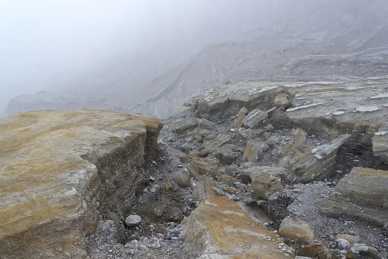 Layered yellow and grey rock inside the Ijen crater in morning mist